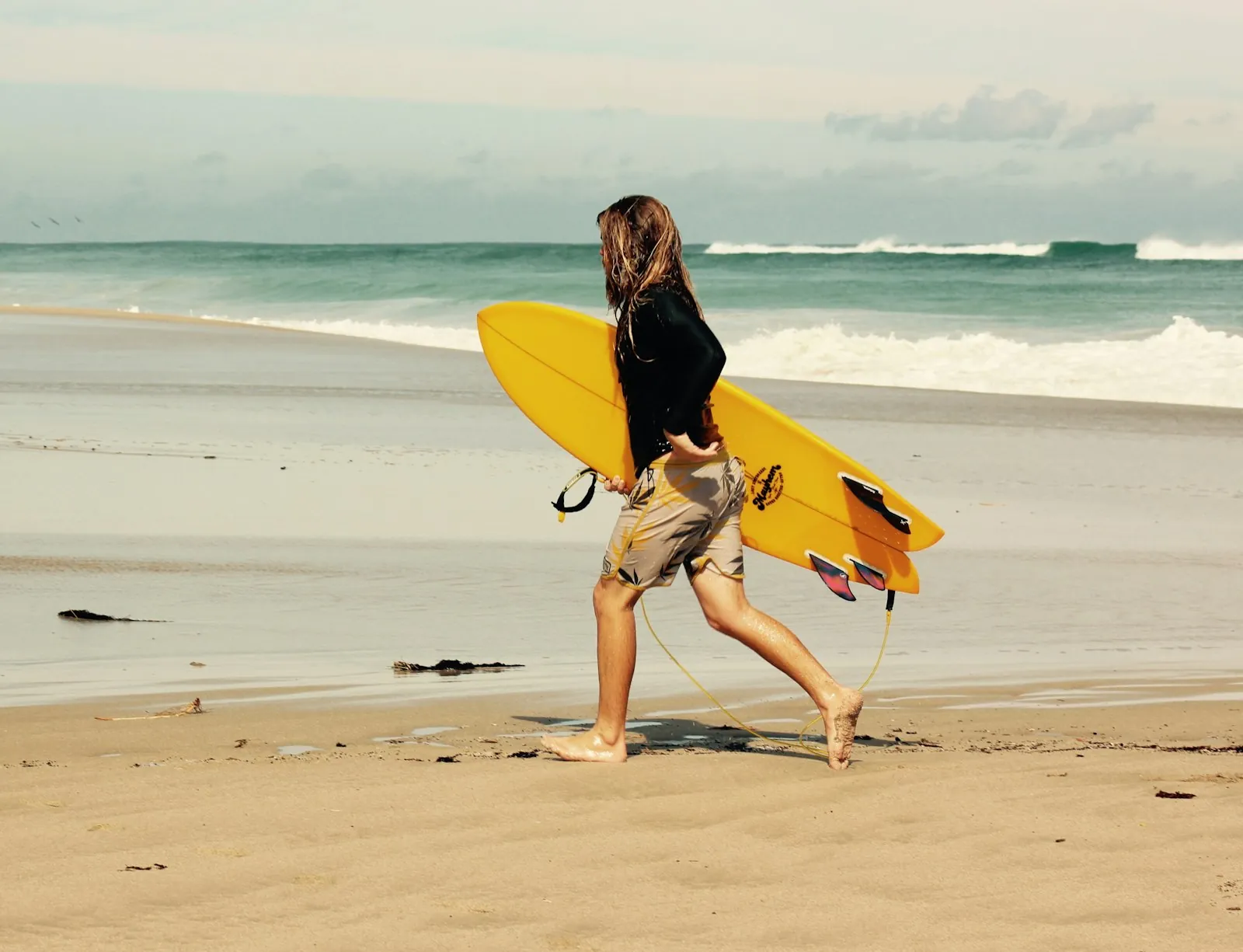 Surfer carrying a yellow board along the beach